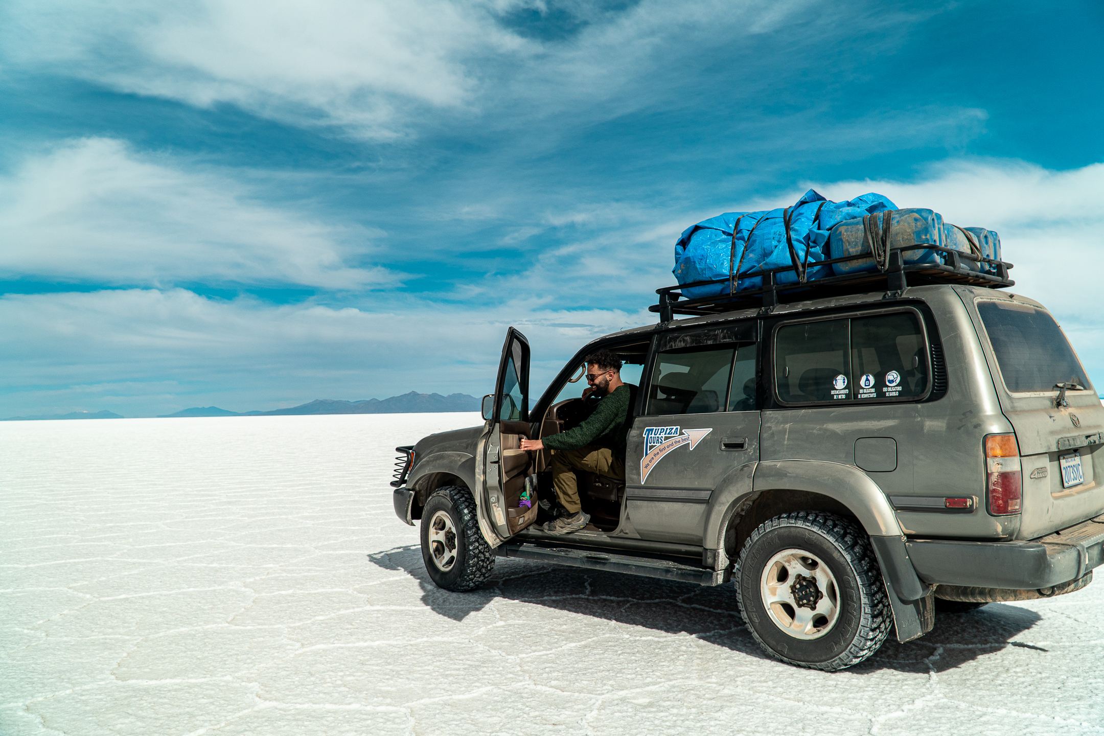 Teal vehicle with surfboards on beach